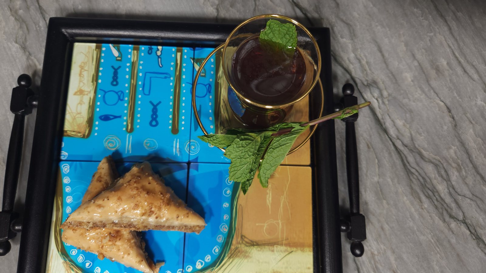 Baklava pieces and a glass of mint tea on a decorative blue tile tray